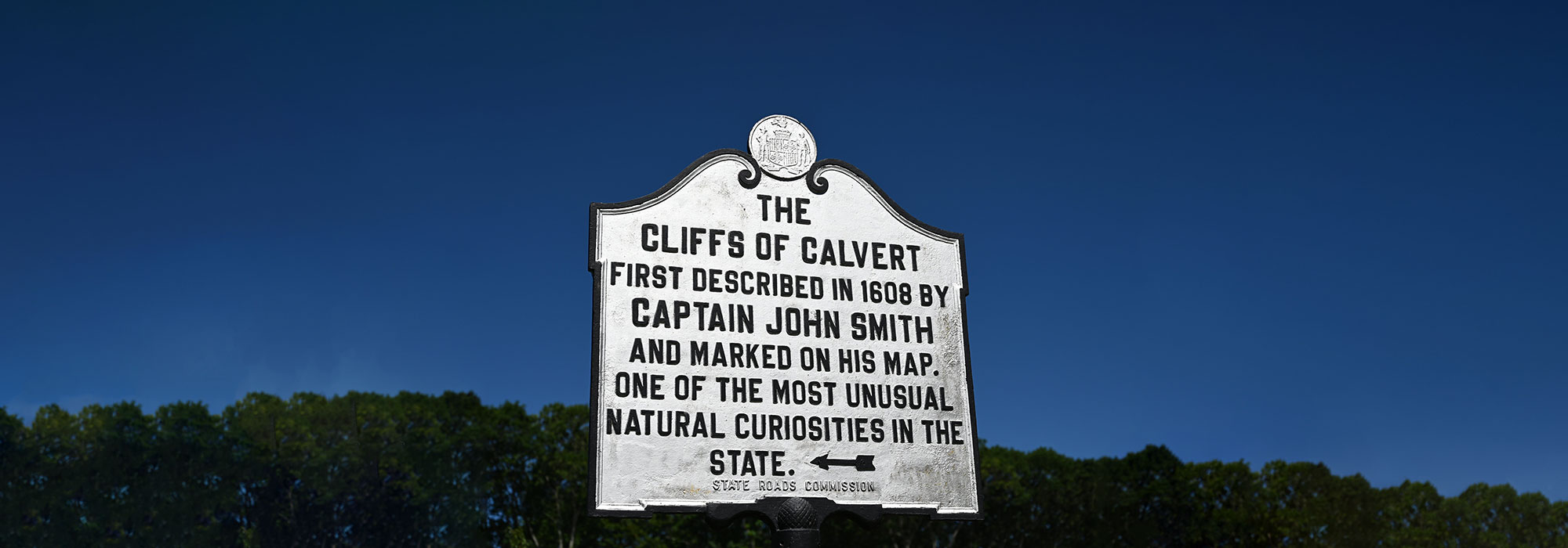 Shows a sign that reads, The Clifffs of Calvert. First Discovered in 1608 by Captain John Smith and marked on his map. One of the most unusual curiosities in the state