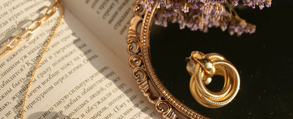 Earing sits on small merror that is resting on top of book. Dryed flowers frame the picture